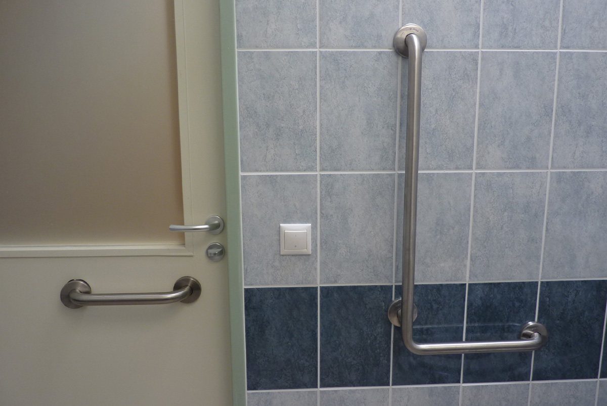Rozsdamentes acél fali kapaszkodó és behúzókar az ajtón. A kilincs alatt WC-zár található - helyesen.